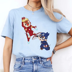 May include: A light blue t-shirt with a cartoon image of two chipmunks dressed as superheroes. One chipmunk is dressed as Iron Man and the other is dressed as Captain America.