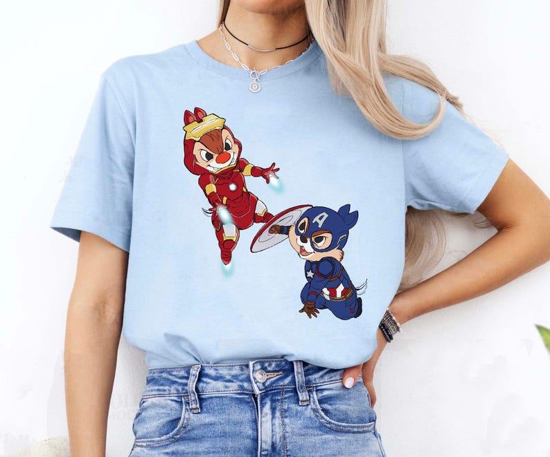 May include: A light blue t-shirt with a cartoon image of two chipmunks dressed as superheroes. One chipmunk is dressed as Iron Man and the other is dressed as Captain America.