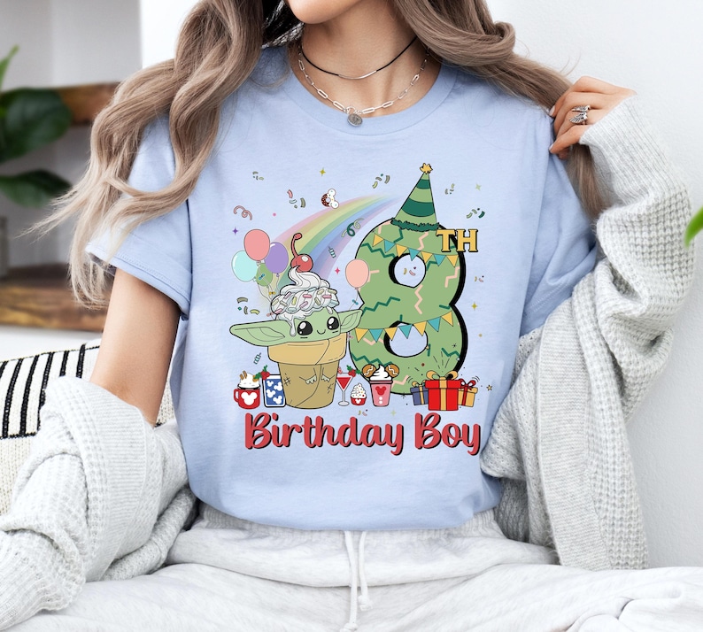 May include: Light blue t-shirt with a green number eight, a rainbow, and a cartoon character holding a cone of ice cream. The text "8th Birthday Boy" is printed on the shirt.