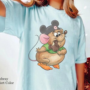 Puede incluir: Camiseta azul claro con un rat&oacute;n de dibujos animados que lleva un sombrero de Mickey Mouse y come un helado con forma de Mickey Mouse. El rat&oacute;n es marr&oacute;n, con una oreja rosa y pies naranjas. La camiseta tiene la inscripci&oacute;n "Chambray Comfort Color".