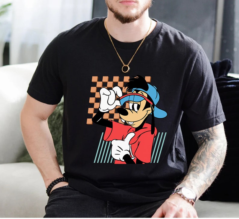 May include: Black t-shirt featuring a cartoon illustration of Goofy wearing a red shirt, blue hat, and sunglasses. Goofy is standing in front of a checkered background with blue and white stripes.