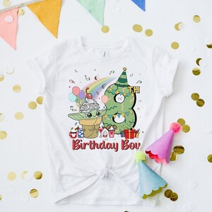 May include: White t-shirt with a green alien character holding a cup of ice cream and a green Christmas tree shaped like the number 8. The text "8th Birthday Boy" is printed on the shirt.