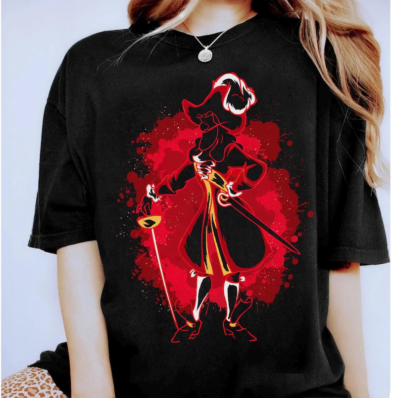 May include: Black t-shirt featuring a red, yellow and white graphic of Captain Hook from Peter Pan. The graphic is in a watercolour style with splashes of red paint.