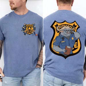 Puede incluir: Camiseta azul claro con una insignia de la polic&iacute;a de Zootr&oacute;polis en la parte delantera y trasera. La parte delantera presenta polic&iacute;as de dibujos animados. La parte trasera muestra un polic&iacute;a b&uacute;falo de dibujos animados. Cuello redondo.