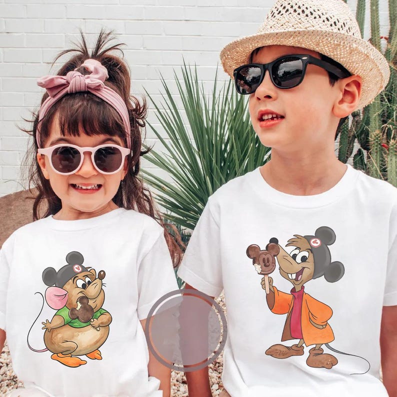 Puede incluir: Dos ni&ntilde;os con camisetas blancas con dibujos de ratones de dibujos animados. La ni&ntilde;a lleva gafas de sol rosas y una diadema a juego. El ni&ntilde;o lleva un sombrero de paja y gafas de sol. Ambas camisetas muestran un rat&oacute;n sosteniendo un helado de chocolate.