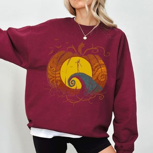 Pode incluir: Camisola de cor bord&ocirc; com um gr&aacute;fico de uma ab&oacute;bora com uma silhueta de Jack Skellington de O Estranho Mundo de Jack em p&eacute; numa colina dentro da ab&oacute;bora.