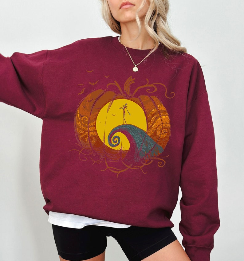 Pode incluir: Camisola de cor bord&ocirc; com um gr&aacute;fico de uma ab&oacute;bora com uma silhueta de Jack Skellington de O Estranho Mundo de Jack em p&eacute; numa colina dentro da ab&oacute;bora.