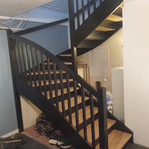 Può includere: Scala in legno nero con corrimano curvo e gradini in legno. La scala si trova in una casa con una parete blu chiaro e un soffitto bianco.