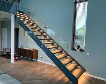 May include: Modern staircase with wooden steps and a dark blue metal frame. The stairs have glass railings and built-in lighting. The interior features a wooden cabinet, a window with blinds, and a light blue wall.
