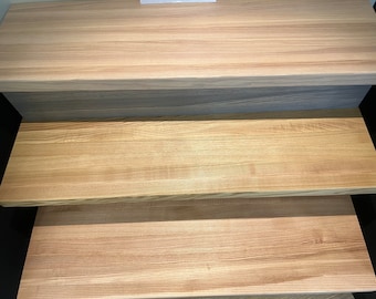 May include: Three wooden steps with a light brown wood grain. The top step is slightly darker than the bottom two steps.