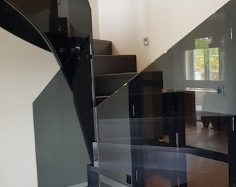May include: Black glass railing with black metal accents on a modern staircase. The glass panels are tinted and reflect the surrounding environment.