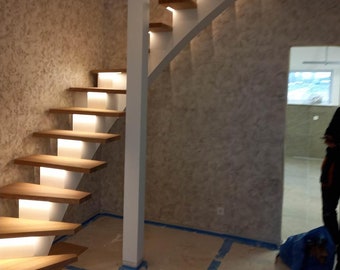 May include: A modern wooden staircase with white railings and built-in LED lights. The staircase is curved and has a white pillar on the left side.