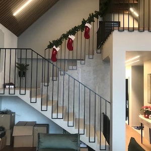Puede incluir: Una escalera moderna con una barandilla de metal negro y una pared blanca. La escalera está decorada con una guirnalda de vegetación y calcetines rojos.