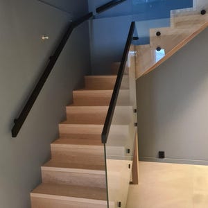 Op de afbeelding: Een houten trap met een glazen en zwarte metalen leuning. De treden zijn gemaakt van licht hout en hebben een natuurlijke afwerking. De leuning is gemaakt van zwart metaal en heeft een modern ontwerp.