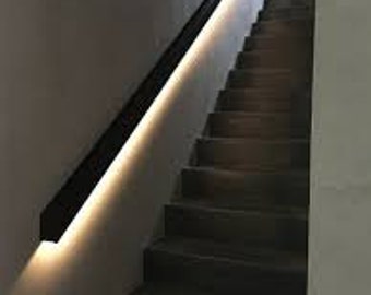 May include: A modern staircase with dark gray steps and a black handrail. The handrail features integrated lighting that casts a warm glow along the wall. The wall is a light gray color.