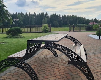 May include: A black metal outdoor table and bench set with intricate cut-out designs. The table and bench are made of metal with a dark brown finish. The set is sitting on a brick patio.