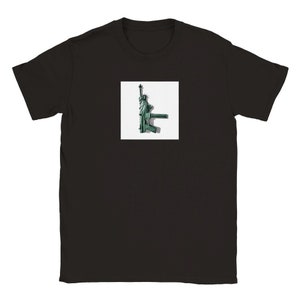 May include: Black t-shirt featuring a square graphic of the Statue of Liberty stylized as a green assault rifle. The graphic is centered on the chest of the shirt. The shirt has short sleeves and a crew neck.