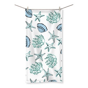 May include: White beach towel featuring a repeating pattern of light blue seashells, starfish, and teal seaweed. The towel is suspended from a clothesline with a wooden peg. The design has a watercolour effect.