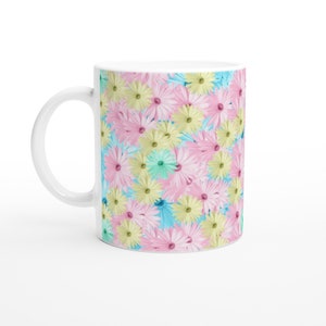 May include: White ceramic mug featuring a repeating floral pattern. The design includes pink, yellow, and blue flowers against a light blue background. The mug has a white handle and a glossy finish.