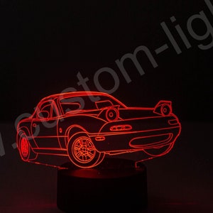 Op de afbeelding: Rood verlicht 3D-geprint model van een Mazda MX-5 sportwagen op een zwarte basis. Het model wordt van binnenuit verlicht, waardoor een gloeiende omtrek van de auto ontstaat.