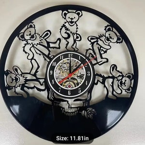 May include: Black wall clock featuring dancing bear silhouettes and a skull design. The clock has a black face with a visible mechanical movement and red hands. The clock measures 11.81 inches in diameter.