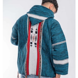May include: A teal and black hooded pullover featuring a central vertical panel with a white stripe, red borders, and black geometric patterns. The sleeves have horizontal white stripes, and the hem includes small decorative hanging tassels.