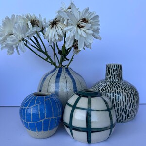 May include: Four ceramic vases of varying shapes and sizes, each with unique patterns. One vase has blue stripes, another has a blue grid, a third has a green grid, and the last has a black and white dotted design. White flowers are in one vase.