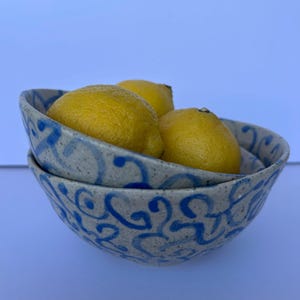 May include: Two ceramic bowls stacked, featuring a blue and white swirl pattern, holding three yellow lemons. The bowls have a speckled texture. The lemons are a vibrant yellow colour.