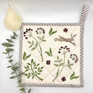 May include: Cream-coloured, square quilted pot holder with a brown rabbit, green leaves, and burgundy floral designs. The border and hanging loop have a grey and white striped pattern.