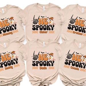 six beige t-shirts with Halloween-themed designs, including a skeleton hand, bats, and the text "NE SPOKEY" and "Sister" printed on them.