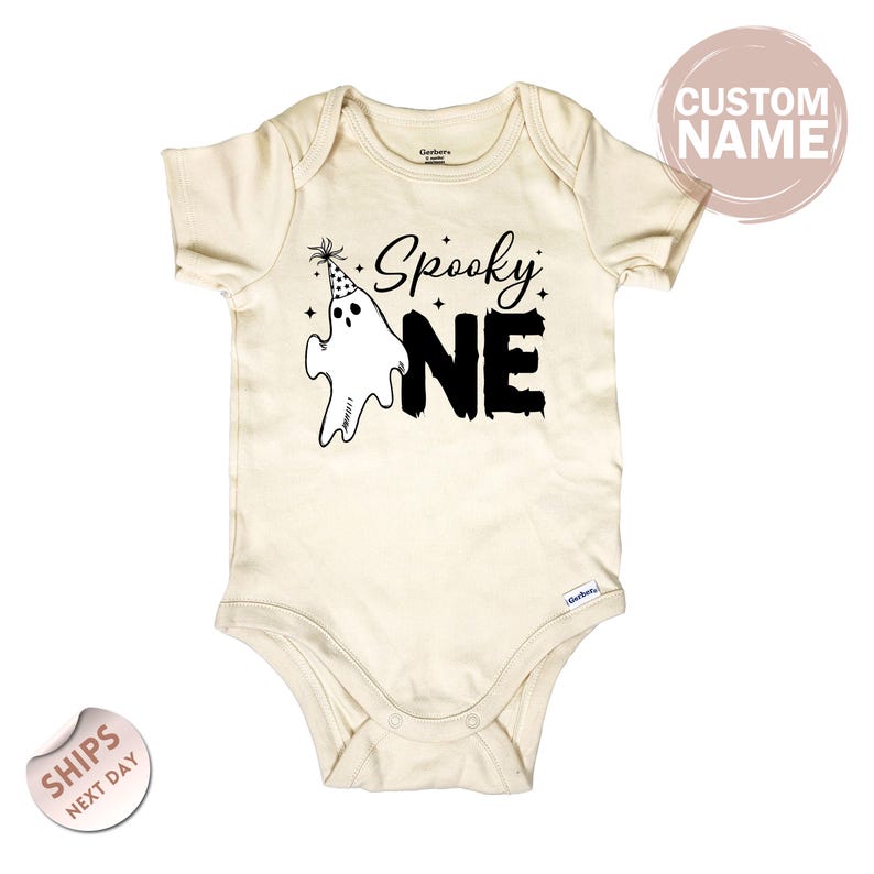 A beige baby onesie with a Halloween-themed design, including a ghost and the text "Spooky one".