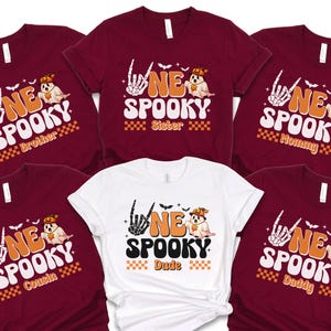 a collection of seven burgundy t-shirts with the same Halloween-themed design, including a skeleton hand and the text "NE SPOKEY SISTER" and "NE SPOKEY Dude".