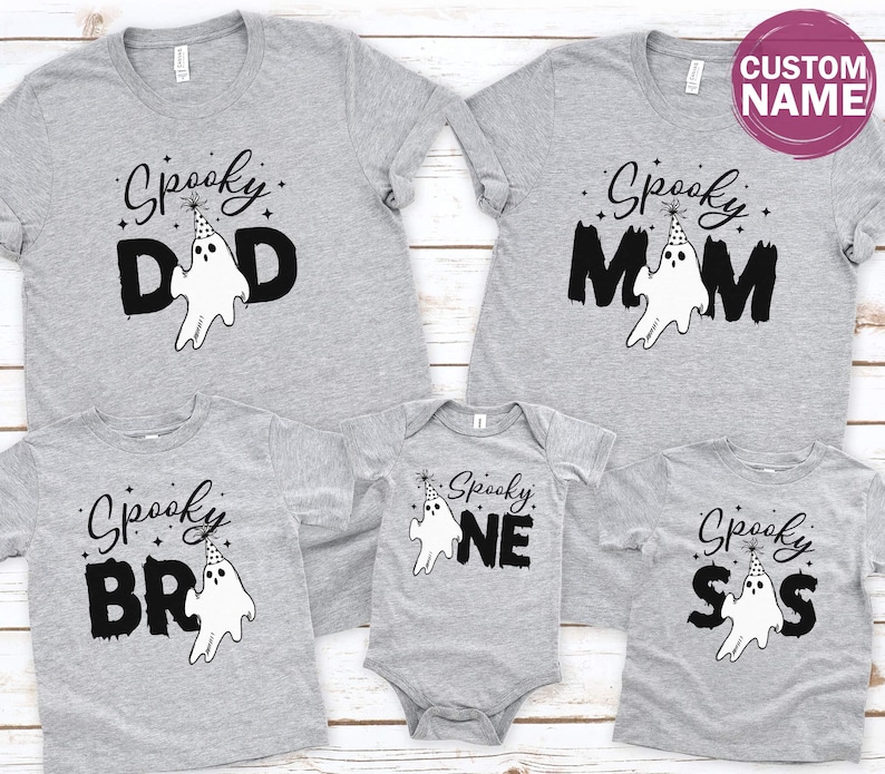a collection of gray t-shirts with the text "Spooky" printed on them, along with various ghost-like designs. The t-shirts appear to be family-sized, suggesting they are intended for a group of people, possibly for a Halloween or themed event.