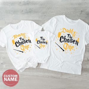 three white t-shirts with the same design, laid out on a wooden surface.