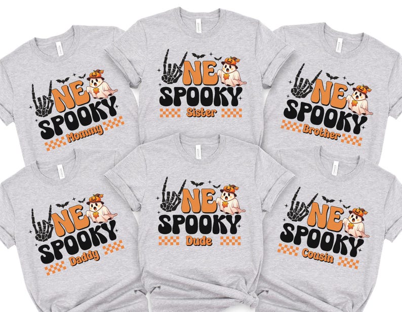A collection of gray t-shirts with Halloween-themed designs, including a skeleton hand, a ghost, and the text "NE SPOKEY" and "Sister" printed on them.