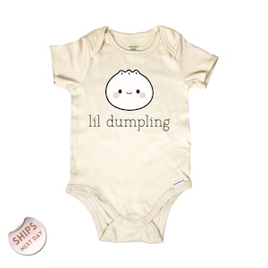 May include: Cream-colored baby onesie with short sleeves. The front features a smiling dumpling graphic with pink cheeks and the text "lil dumpling" in black. The onesie is made of soft material and has snap closures.