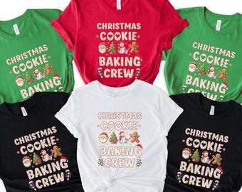 May include: A collection of short-sleeved t-shirts in various colors, including red, green, black, and white. Each shirt features the text "CHRISTMAS COOKIE BAKING CREW" with festive illustrations of Santa, a Christmas tree, a snowman, and a gingerbread man.