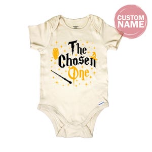 A white onesie with a printed design featuring the text "The Chosen One" and a wand.