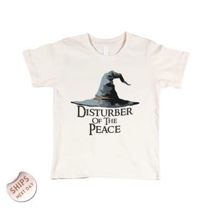 A white t-shirt with a graphic design of a wizard's hat and the text "Disturbance of the Peace" printed on it.