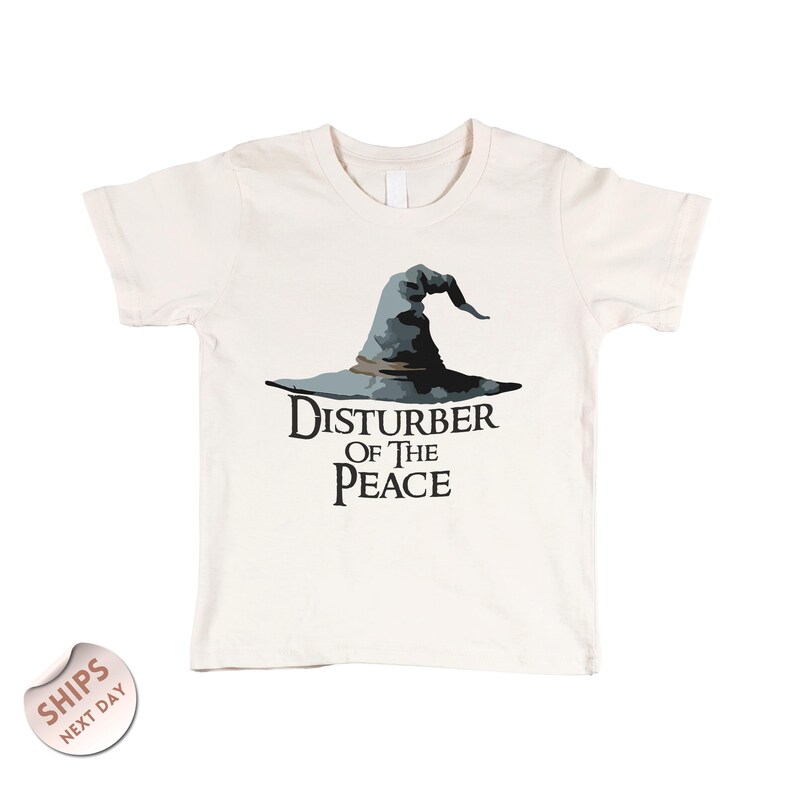 A white t-shirt with a graphic design of a wizard's hat and the text "Disturbance of the Peace" printed on it.