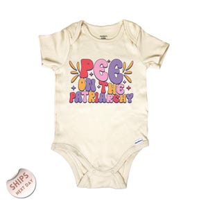 May include: Cream-colored baby bodysuit with short sleeves. The front features the text "PEE ON THE PATRIARCHY" in a retro font with pink, purple, orange, and yellow colors. The bodysuit has a snap closure.