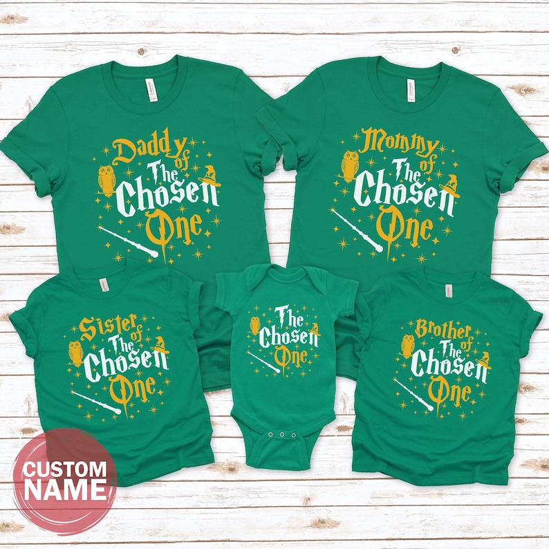 A collection of green t-shirts with the text "The Chosen One" printed on them, along with the names "Daddy", "Mommy", "Sister", "Brother", and "Brother of the Chosen One".