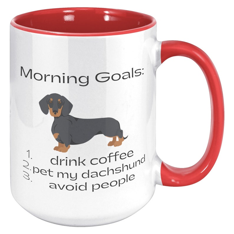 May include: White coffee mug with a red rim and handle. The mug has a black and tan dachshund illustration and the text "Morning Goals: 1. drink coffee 2. pet my dachshund 3. avoid people".