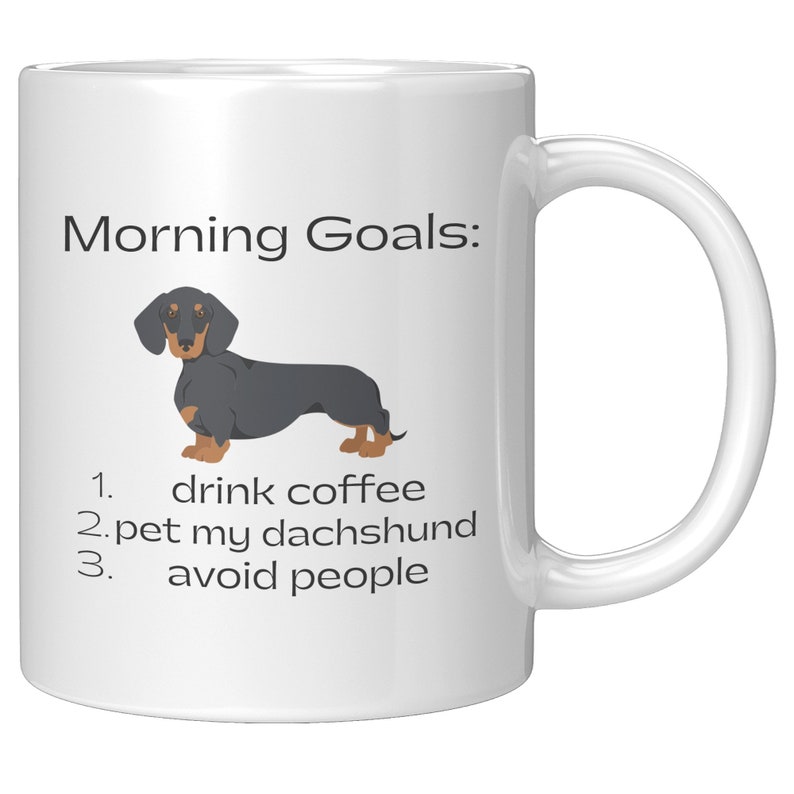 May include: White coffee mug with a black and tan dachshund illustration and the text "Morning Goals: 1. drink coffee 2. pet my dachshund 3. avoid people"