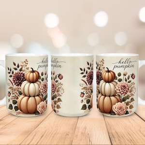 Op de afbeelding: Een witte keramische mok met een herfstthema. Het ontwerp toont een stapel pompoenen, bloemen en de tekst "hello pumpkin". De mok heeft een wit handvat en staat tegen een vage achtergrond.