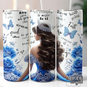 May include: A white tumbler featuring a blue floral design, butterflies, and inspirational text. The design includes a woman in a blue gown and crown. The tumbler has a straw and is decorated with the words "good vibes" and "faith".