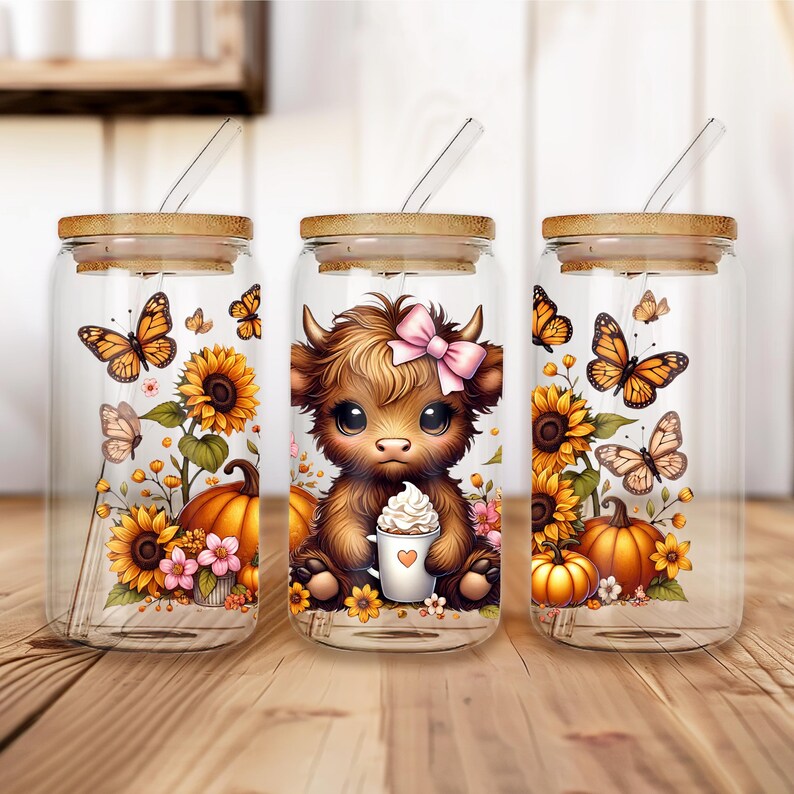 May include: Three glass tumblers with bamboo lids and glass straws. Each tumbler features a different design: butterflies, sunflowers, pumpkins, and a Highland cow with a pink bow holding a coffee cup. The tumblers are on a wooden surface.