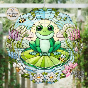 May include: A stained glass frog design with a smiling green frog on a lily pad, surrounded by flowers and bees. The design is circular with a blue sky background. Text on the image says "2 Free Designs Included" and "ABODE art digital".
