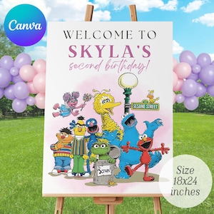 May include: A white welcome sign on an easel, featuring Sesame Street characters and the text "Welcome to Skyla's second birthday!" The sign is 18x24 inches and includes a Canva logo. Balloons in pink and purple are in the background.