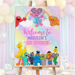 K&ouml;nnte beinhalten: Ein farbenfrohes Geburtstagsplakat mit Sesamstra&szlig;en-Figuren. Auf dem Schild steht "Welcome to Madison's 2nd Birthday!" vor einem Regenbogen- und Sternenhintergrund. Das Schild wird auf einer Holzstaffelei pr&auml;sentiert.